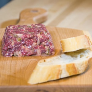 Un tartare de viande sur une planche de bois.