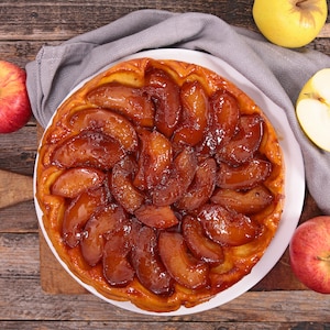 Une tarte Tatin entourée de quelques pommes.