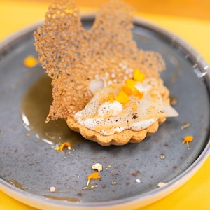 Une tartelette garnie de crème et d'un morceau de crêpe fine et croustillante, dans une assiette.