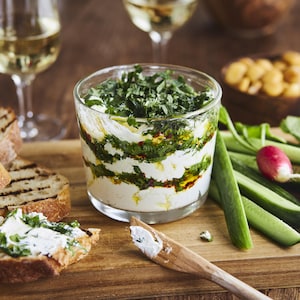 Tartinade étagée de fromage de chèvre aux herbes et à l’huile d’olive dans un plat en verre.