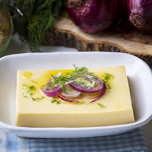 Un morceau de terrine de gourganes dans une assiette. Il est servi avec des échalotes, de l'aneth ainsi que de l'huile d'olive.