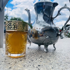 Un verre de thé à la menthe et une théière marocaine.