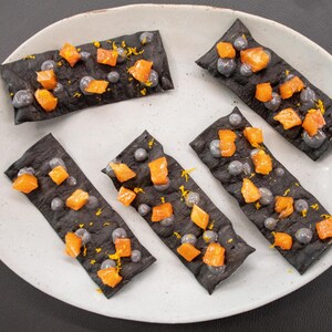 Des cubes de poisson mariné et des boules de yogourt à l'encre de seiche sur des craquelins à l'encre de seiche.