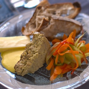 Un morceau de végé-pâté dans une assiette accompagné de légumes, de croûtons et d'une sauce jaune.