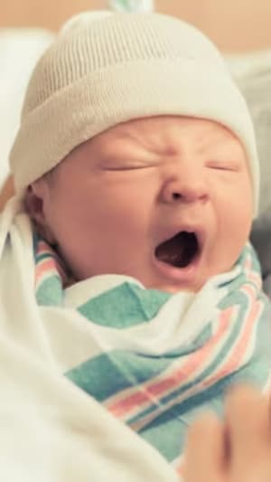 Un bébé baille dans les bras d'une femme.