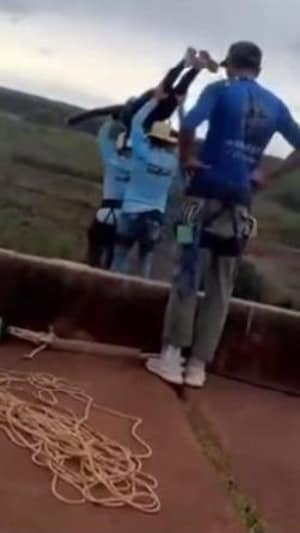 Deux hommes portent à bout de bras une femme munie d'un casque. Umn autre les regarde, une corde à ses pieds.