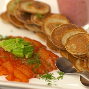 Des blinis et des tranches de saumon gravlax sur une grande assiette.