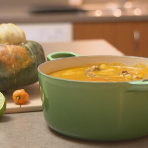 Un chaudron de soupe joumou et une courge giraumon sur un comptoir de cuisine.