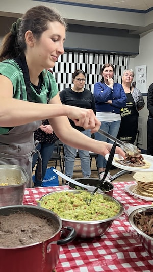 Une femme tient une assiette avec un taco, d'autres femmes la regarde derrière.