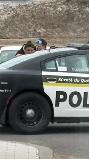 Un homme placé en état d'arrestation près d'un véhicule de patrouille de la Sûreté du Québec.