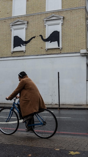 Une femme passe à vélo devant une œuvre d'art représentant deux éléphants, prétendument réalisée par Banksy, sur un immeuble résidentiel, le 6 août 2024 dans le quartier de Chelsea à Londres, en Angleterre.