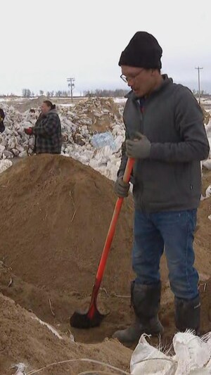Un bénévole tient une pelle pour aménager une barrière constituée de sacs de sable à Peguis. D'autres bénévoles positionnent les sacs de sable afin de consolider les barrières.