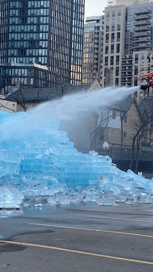 Un pompier sur une échelle arrose le bloc de glace dans un stationnement.