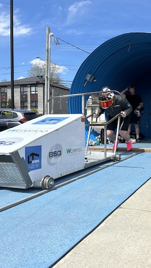 Un homme s'apprête à pousser le bobsleigh sur un rail, sous le regard de plusieurs personnes rassemblées autour.