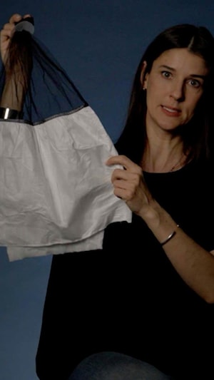 La journaliste est assise dans un studio. Elle regarde l'objectif de la caméra. Elle tient un masque anticrachat afin de le montrer à la caméra. 