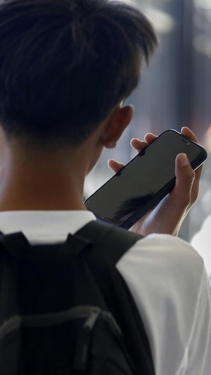 Un élève écoute son cellulaire devant la fenêtre d'une école (Photo d'archives)
