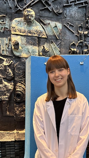 L'étudiante Amy Gudmundson  pose en blouse blanche devant le logo de l'université du Manitoba.