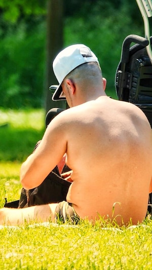 Un homme est assis dans l'herbe au soleil près d'un fauteuil roulant.                 