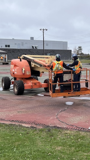 Deux ouvriers dans la nacelle d'une plate-forme élévatrice orange travaillent sur un terrain en chantier.
