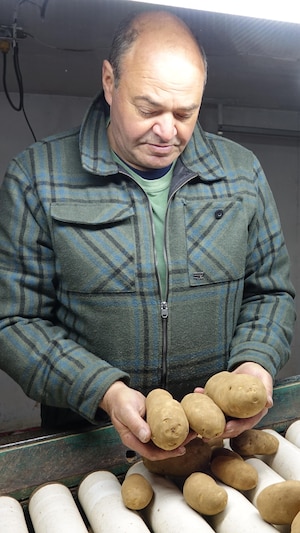 Une photo de Christian Poirier, dans ses installations. Il tient dans ses mains trois pommes de terre.