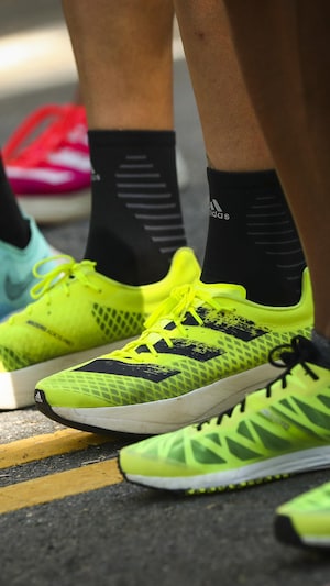 Gros plan sur les pieds de trois athlètes, chaussés par des souliers de course aux couleurs vives.