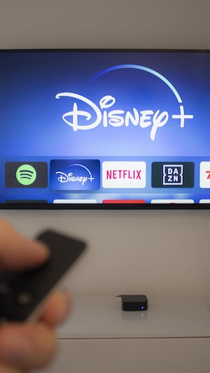 Une main tient une télécommande face à une télévision qui montre Disney+.