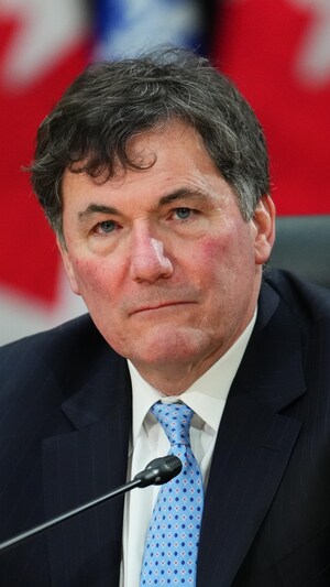 Dominic LeBlanc, l'air sérieux, lors d'une conférence de presse devant des drapeaux canadiens.