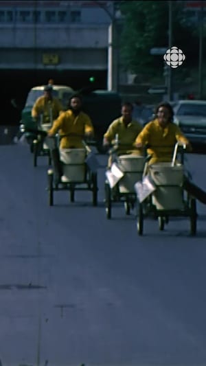 Des hommes en uniformes jaunes à bord de vélos triporteurs munis de poubelles circulent sur une rue.