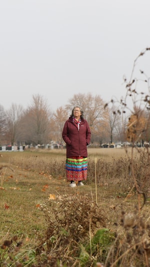 Une femme est devant un cimetière, elle regarde au loin. 