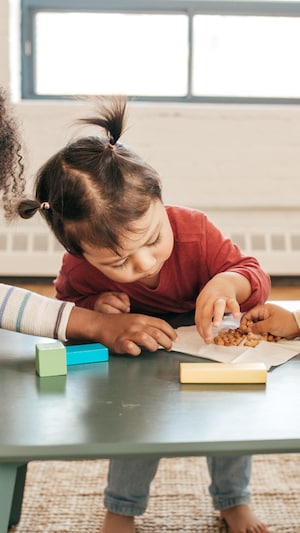 Trois enfants en bas âge mangent une collation autour d'une table basse.