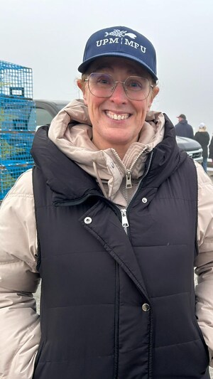 Une femme souriante devant un quai, des casiers de homards derrière elle. 