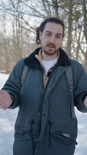 Un homme avec un manteau se tient dehors dans une forêt durant l'hiver.