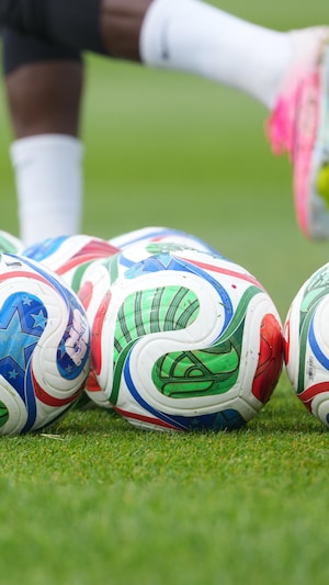 Des ballons aux couleurs de la Coupe du monde au premier plan alors que des joueurs de l'équipe de soccer masculine du Canada pratiquent.