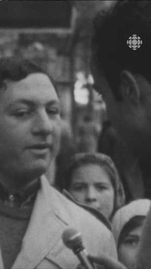 Pierre Nadeau vu de dos qui tend le micro à un jeune homme parisien dans la rue. 