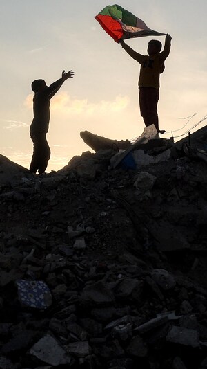 Un garçon brandit un drapeau palestinien au sommet d’un tas de gravats dans un camp de personnes déplacées par le conflit à Bureij, dans le centre de la bande de Gaza, le 17 janvier 2025, après l’annonce d’une trêve au milieu de la guerre en cours entre Israël et le Hamas.