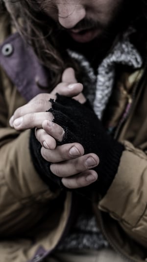 Un homme sur un trottoir se frotte les mains pour se réchauffer. 