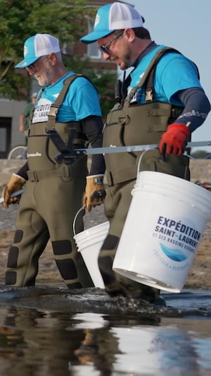 Deux hommes ramassent des déchets dans le fleuve Saint-Laurent.