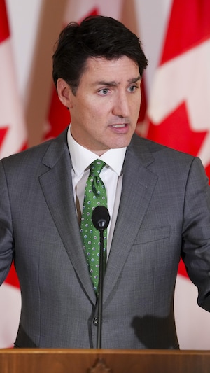 Justin Trudeau parlant devant plusieurs drapeaux canadiens.