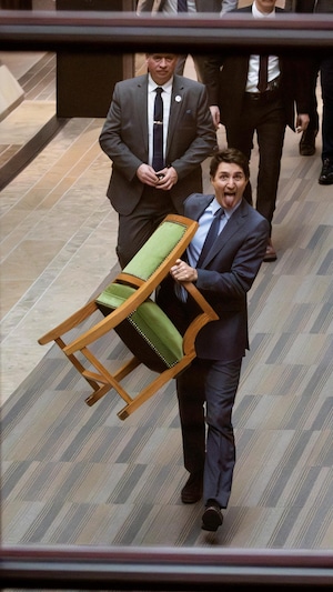 Justin Trudeau tire la langue en marchant avec son fauteil dans les mains.