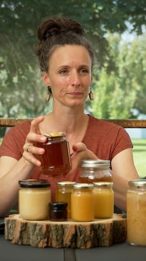 Une femme montre des pots de miel de différentes couleurs et grosseurs.