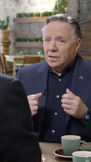 François Legault assis dans un café, une tasse devant lui sur la table.