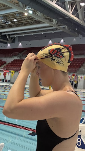 Une nageuse est à l'extérieur de la piscine et met ses lunettes. 