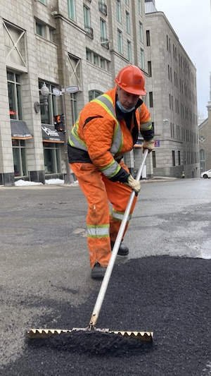 Un employé épand de l'asphalte sur un nid-de-poule.