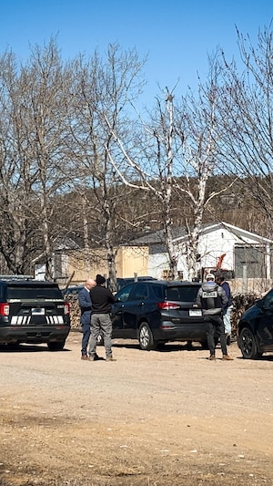 Plusieurs policiers de la Sûreté du Québec et des civils sont rassemblés près de véhicules sur un terrain de terre, à Longue-Rive.