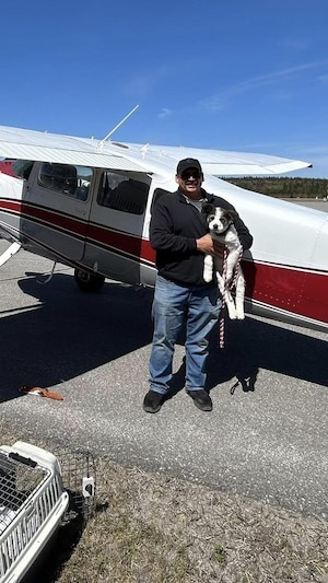 Paul Ricklef devant son avion avec un chien dans ses bras. 