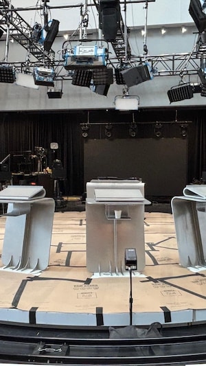 Quatre lutrins placés en demi-cercle sur un plateau de télévision.