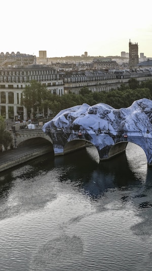 Cette photographie aérienne, prise le 1er juin 2026, montre l'installation de « La caverne du Pont-Neuf », la dernière œuvre de l'artiste JR, sur le Pont-Neuf à Paris. On voit le pont transformé complètement en une longue caverne composée de roches et faite de toiles et d'espaces ouverts. 