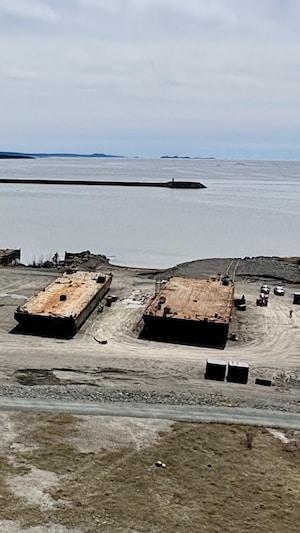 Des employées réparent 2 barges sur un terrain vague au port de Cacouna.  