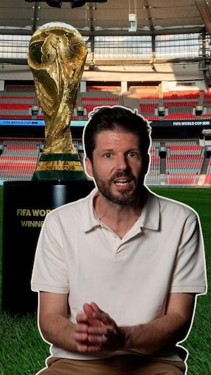 Il s'agit d'un montage de deux photos. En arrière-plan, un stade de soccer avec le trophée du vainqueur de la Coupe de monde de la FIFA. En avant-plan, un homme, le journaliste Romain Schué, il regarde l'objectif de la caméra en mode explication. 