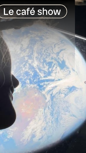 Contre-plongée d'une femme à contrejour qui regarde la terre à travers le hublot d'une capsule spatiale.